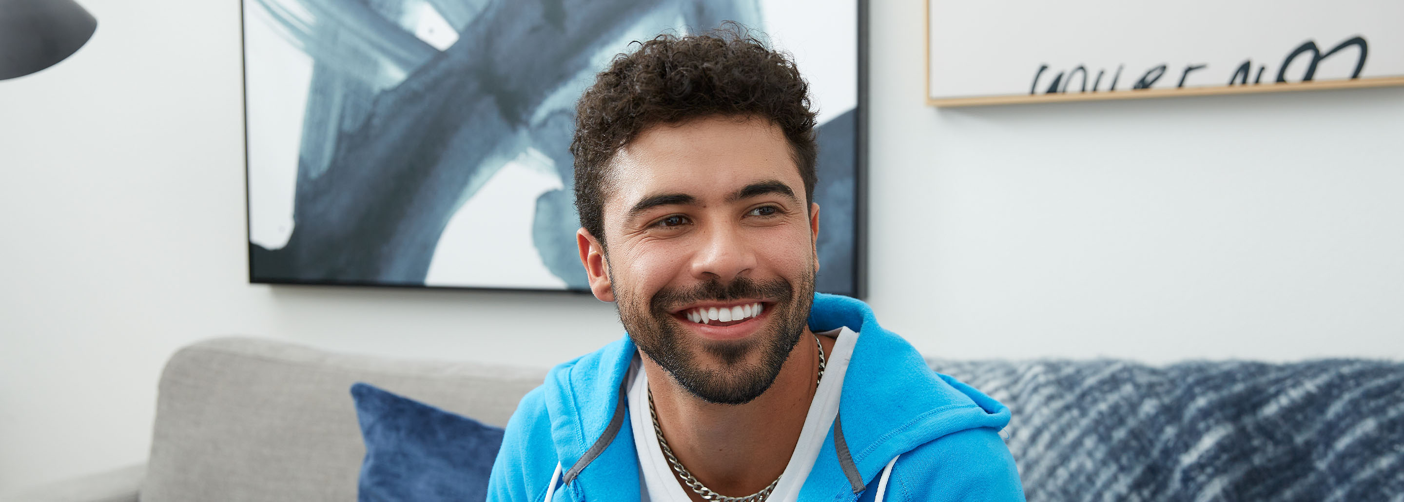 Curly-haired brunette man smiles bright as he looks ahead.