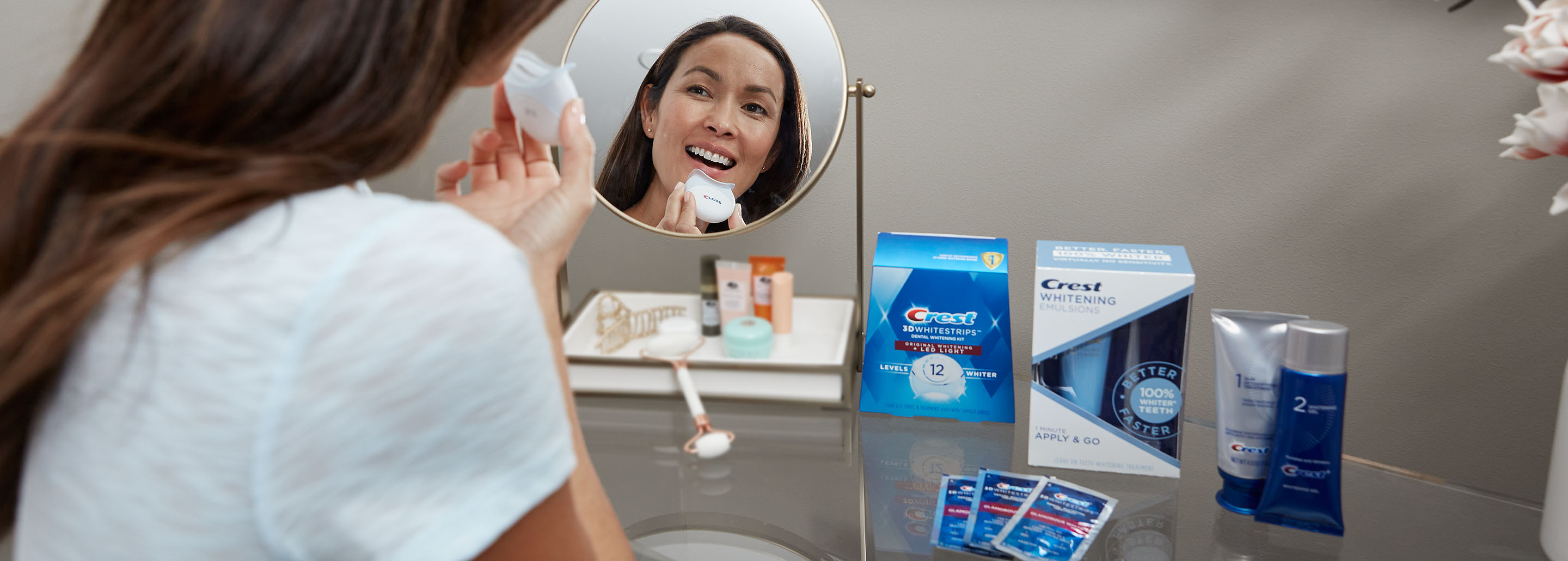 Woman smiles looking into her vanity mirror as she begins to use the Crest LED Light.